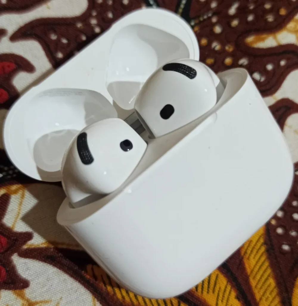 AirPods 4 trong hộp sạc đang mở, đặt trên vải hoa văn
