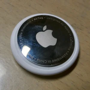 AirTag, mặt thép in logo Apple, đặt trên bàn gỗ