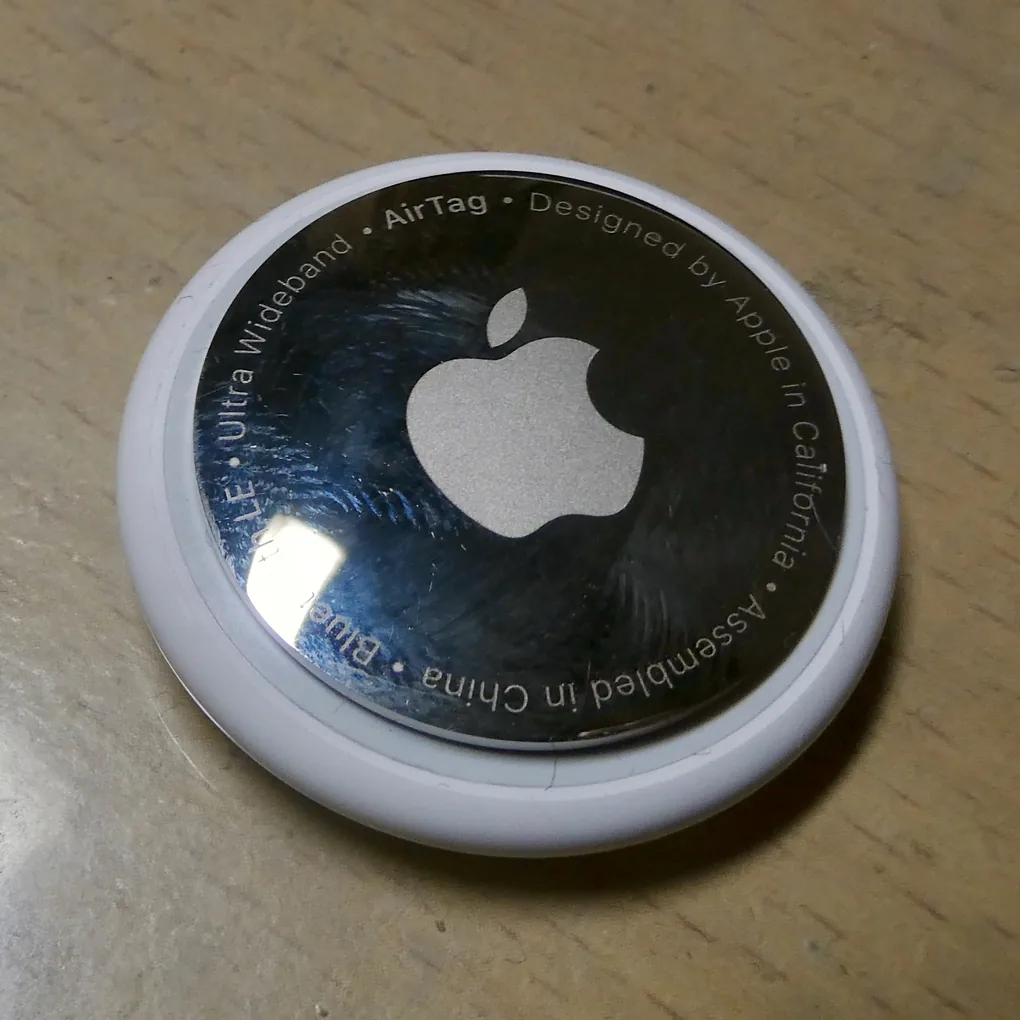 AirTag, mặt thép in logo Apple, đặt trên bàn gỗ